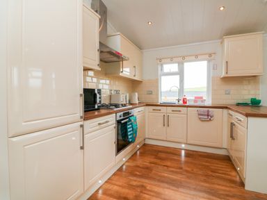 A kitchen with white cabinets wooden countertops a microwave an oven a gas stove a window a sink and wooden flooring at Ridge's Retreat No 7 Kigbeare Lodges Ashbury Resort near Fowley Cross Sourton Down and Okehampton