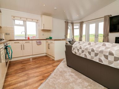 A kitchen with cream cabinets and wooden floor connected to a living area with sofas and curtains at Ridge's Retreat No 7 Kigbeare Lodges in Ashbury Resort near Fowley Cross Sourton Down and Okehampton