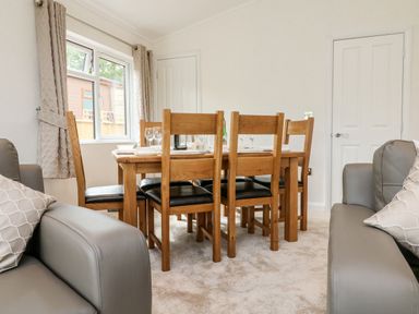A dining area with a wooden table and six chairs next to gray sofas and a window with curtains at Ridge's Retreat No 7 Kigbeare Lodges Ashbury Resort near Fowley Cross Sourton Down and Okehampton