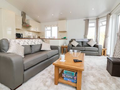 A living room with two gray sofas a wooden coffee table with board games and a kitchen area at Ridge's Retreat No 7 Kigbeare Lodges Ashbury Resort near Fowley Cross Sourton Down and Okehampton