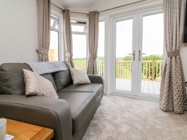 A sofa with cushions next to windows and glass doors leading to a balcony at Ridge's Retreat No 7 Kigbeare Lodges Ashbury Resort near Fowley Cross Sourton Down and Okehampton