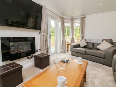 A living room with a sofa two ottomans a wall-mounted TV and fireplace wooden coffee table with cups and remote at Ridge's Retreat No 7 Kigbeare Lodges Ashbury Resort near Fowley Cross Sourton Down and Okehampton