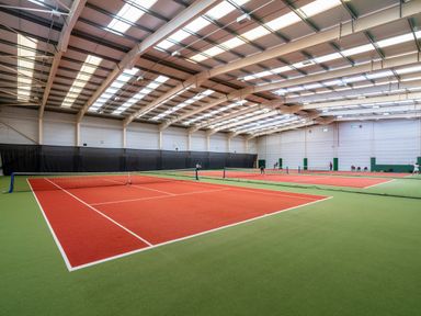An indoor sports facility with multiple red and green tennis courts and players at Ridge's Retreat No 7 Kigbeare Lodges Ashbury Resort near Fowley Cross Sourton Down and Okehampton