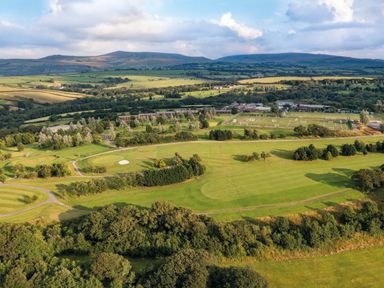 An aerial view of a green landscape with golf course, sports fields, buildings, trees, and hills in the background at Ridge's Retreat No 7 Kigbeare Lodges Ashbury Resort near Fowley Cross Sourton Down and Okehampton