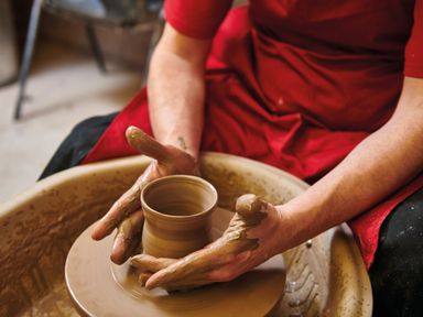 A person shaping clay on a pottery wheel wearing a red apron at Ridges Retreat No 7 Kigbeare Lodges Ashbury Resort near Fowley Cross Sourton Down and Okehampton