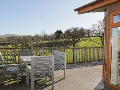 A wooden deck with table and chairs overlooking green fields and trees at Ridges Retreat No 7 Kigbeare Lodges Ashbury Resort near Fowley Cross Sourton Down and Okehampton