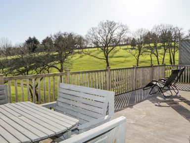 A wooden deck with a table, benches, and reclining chairs overlooking a grassy hillside with trees at Ridge's Retreat No 7 Kigbeare Lodges Ashbury Resort near Fowley Cross Sourton Down and Okehampton