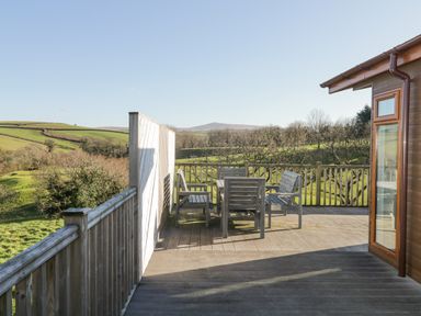 An outdoor wooden deck with a table and chairs overlooking green fields at Ridge's Retreat No 7 Kigbeare Lodges Ashbury Resort near Fowley Cross Sourton Down and Okehampton