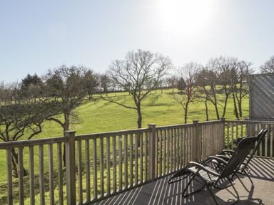 A wooden balcony with two black lounge chairs overlooking a grassy field with scattered trees at Ridge's Retreat No 7 Kigbeare Lodges Ashbury Resort near Fowley Cross Sourton Down and Okehampton