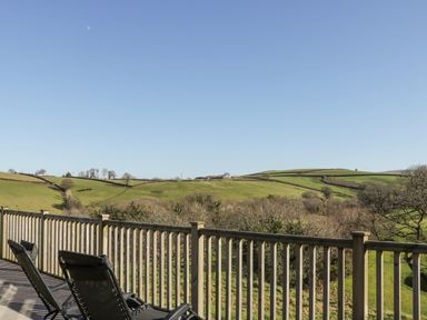 A wooden balcony with two lounge chairs overlooking green rolling hills at Ridge's Retreat No 7 Kigbeare Lodges Ashbury Resort near Fowley Cross Sourton Down and Okehampton