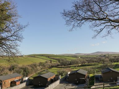 A view of wooden lodges with parking areas and fenced yards overlooking green fields and hills at Ridge's Retreat No 7 Kigbeare Lodges Ashbury Resort near Fowley Cross Sourton Down and Okehampton