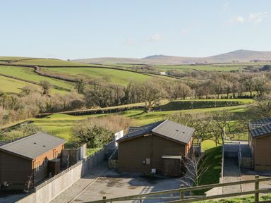 Wooden lodges with fenced yards overlooking green fields and hills at Ridge's Retreat No 7 Kigbeare Lodges Ashbury Resort near Fowley Cross Sourton Down and Okehampton