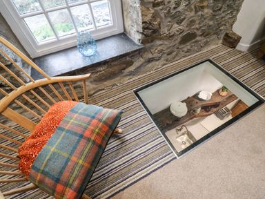 A wooden chair with a blanket near a window and a glass floor panel showing a kitchen below at Plas Glan Yr Afon in Llangernyw