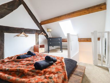 A bedroom with a bed covered with an orange patterned blanket and black towels wooden beams and a chest of drawers at Plas Glan Yr Afon in Llangernyw