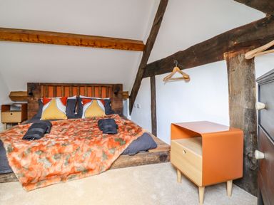 A bedroom with a wooden bed frame orange and gray bedding an orange side table and exposed wooden beams at Plas Glan Yr Afon in Llangernyw