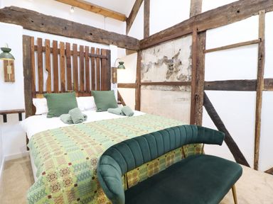 A bedroom with a bed green pillows and a green patterned blanket with exposed wooden beams at Plas Glan Yr Afon in Llangernyw