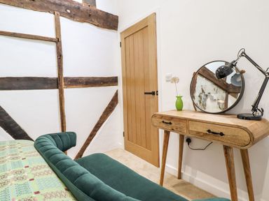 A corner of a room with a wooden door a wooden dressing table with a round mirror and a green vase and a green upholstered chair at Plas Glan Yr Afon in Llangernyw
