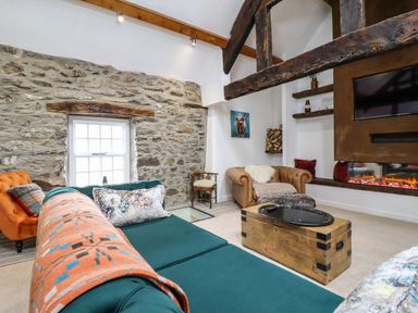 A living room with stone walls wooden beams a teal sofa an orange armchair a brown leather chair a wooden trunk coffee table and a fireplace at Plas Glan Yr Afon in Llangernyw