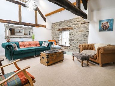 A living room with a green sofa, brown leather sofa, wooden trunk coffee table, stone wall, and exposed wooden beams at Plas Glan Yr Afon in Llangernyw