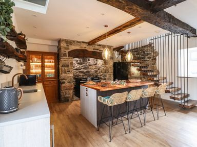A kitchen with a central island and bar stools near a stone wall and staircase at Plas Glan Yr Afon in Llangernyw