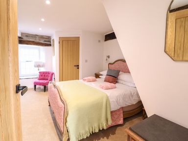 A bedroom with a double bed a pink armchair and wooden door at Plas Glan Yr Afon in Llangernyw