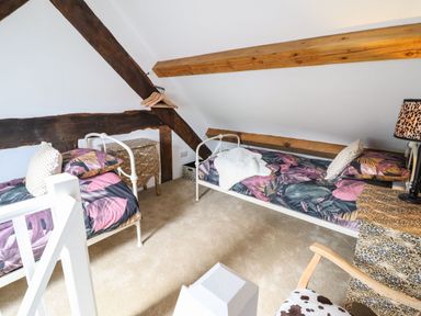 A bedroom with two single beds with purple and green leaf patterned bedding and wooden beams on the ceiling at Plas Glan Yr Afon in Llangernyw
