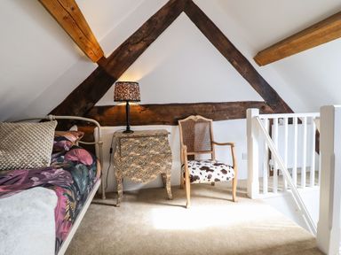 An attic room with a bed a leopard print nightstand a chair with a patterned cushion and wooden beams at Plas Glan Yr Afon in Llangernyw