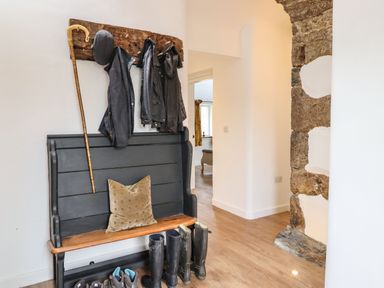 A hallway with a wooden bench with coats and a cane hanging above and boots below at Plas Glan Yr Afon in Llangernyw