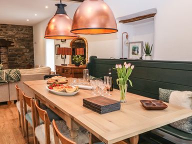 A dining table with plates of food glasses and flowers in a room with stone wall and wooden furniture at Plas Glan Yr Afon in Llangernyw