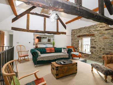 A living room with exposed wooden beams a green sofa wooden chairs a stone wall and a wooden chest at Plas Glan Yr Afon in Llangernyw
