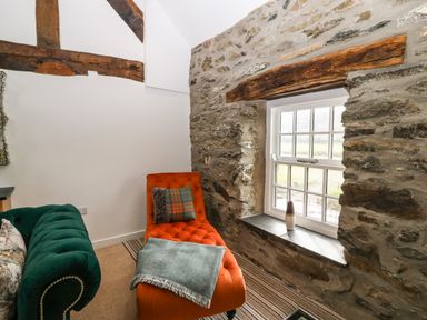 A room with a green sofa and an orange chaise lounge near a window with stone walls at Plas Glan Yr Afon in Llangernyw