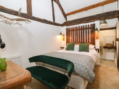 A bedroom with a double bed green pillows a floral bedspread a green bench a wooden headboard and wooden beams at Plas Glan Yr Afon in Llangernyw