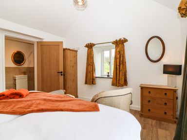 A bedroom with a bed covered with an orange blanket a wooden dresser a chair and a window with curtains at Plas Glan Yr Afon in Llangernyw