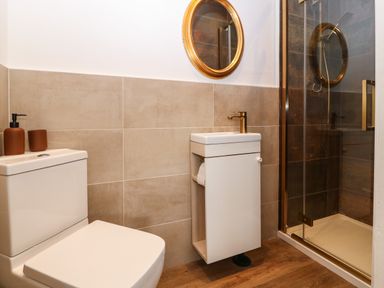 A bathroom with a toilet a sink with a cabinet a round mirror and a glass shower enclosure at Plas Glan Yr Afon in Llangernyw