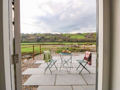 A patio with two chairs and a small table set with drinks and pastries overlooking a green landscape at Plas Glan Yr Afon in Llangernyw