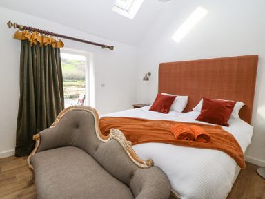 A bedroom with a double bed with orange headboard and cushions a grey loveseat and dark green curtains at Plas Glan Yr Afon in Llangernyw
