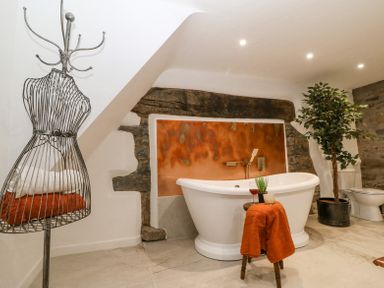 A bathroom with a freestanding bathtub, a stool with a towel and candle, a plant in a pot, and a wire dress form with towels at Plas Glan Yr Afon in Llangernyw