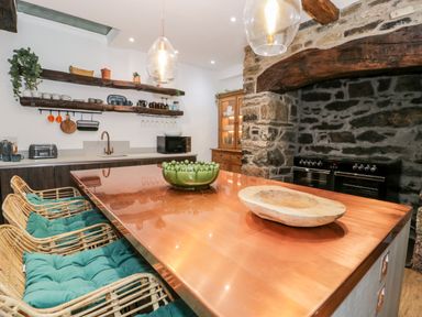 A kitchen with a copper countertop island and wicker chairs with cushions at Plas Glan Yr Afon in Llangernyw