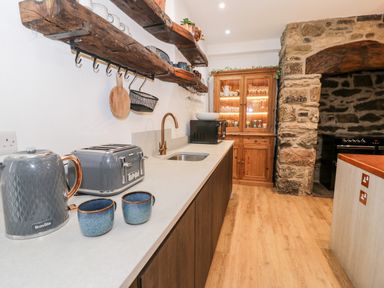 A kitchen with wooden shelves utensils a toaster kettle cups sink and a wooden cabinet with glassware at Plas Glan Yr Afon in Llangernyw