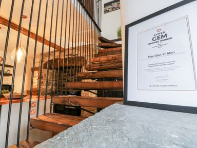 A framed award certificate on a stone ledge next to wooden stairs with metal railings in a kitchen at Plas Glan Yr Afon in Llangernyw