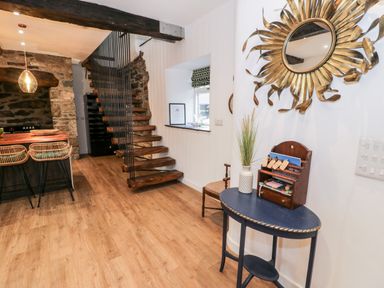 An entryway with a wooden staircase kitchen bar stools and a sunburst mirror at Plas Glan Yr Afon in Llangernyw