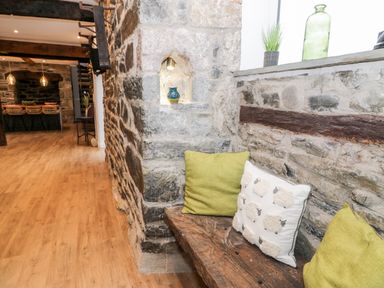 A stone wall corner with a wooden bench with cushions and a small decorative shelf in a rustic interior at Plas Glan Yr Afon in Llangernyw