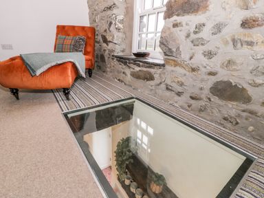 A room with a stone wall and window with a glass floor panel reflecting a window and plants at Plas Glan Yr Afon in Llangernyw