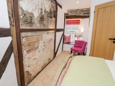 A bedroom corner with an exposed wooden beam wall a pink chair a window with a red blind and a wooden door at Plas Glan Yr Afon in Llangernyw