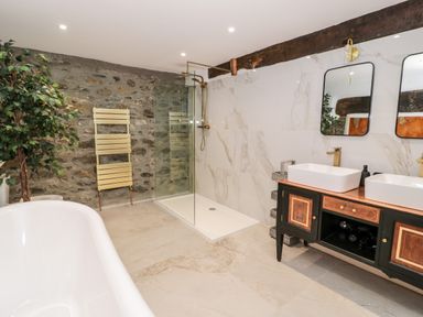 A bathroom with a bathtub a stone wall a glass shower enclosure a double sink vanity with mirrors at Plas Glan Yr Afon in Llangernyw