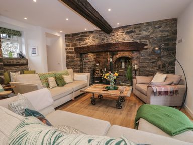 A living room with beige sofas and a wooden coffee table in front of a stone wall fireplace at Plas Glan Yr Afon in Llangernyw