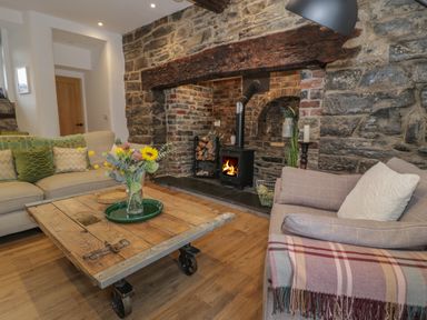 A living room with a wood stove in a stone fireplace two sofas a wooden coffee table with flowers on it at Plas Glan Yr Afon in Llangernyw
