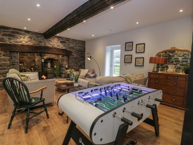 A living room with a foosball table sofas a wooden chair a stone fireplace and a wooden dresser with a mirror at Plas Glan Yr Afon in Llangernyw