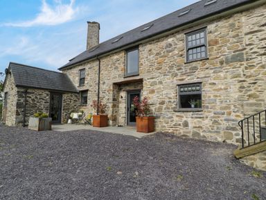 Stone house with slate roof and chimney with gravel driveway and potted plants at Plas Glan Yr Afon in Llangernyw