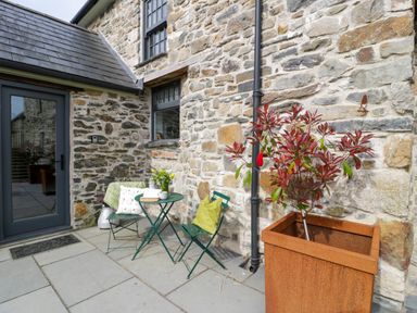 An outdoor seating area with a green table and chairs next to a stone wall at Plas Glan Yr Afon in Llangernyw